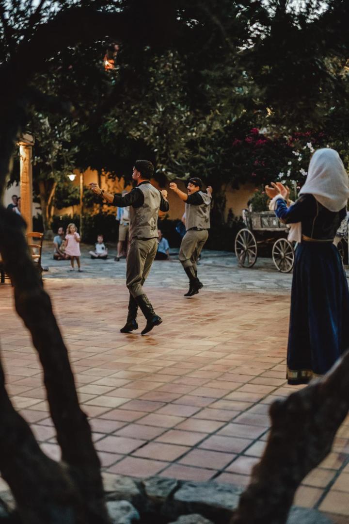 Candia Park Village viesnīcas grieķu vakara priekšnesums Krētā ar dejotājiem tradicionālos tērpos uz flīzēta āra laukuma koku ēnā