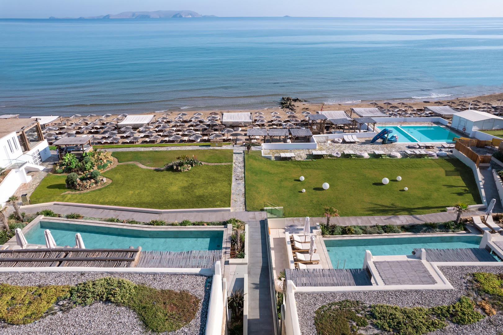 Mitsis Rinela Beach Resort skats no augšas uz privāto pludmali, zālājiem un vairākiem peldbaseiniem piekrastē