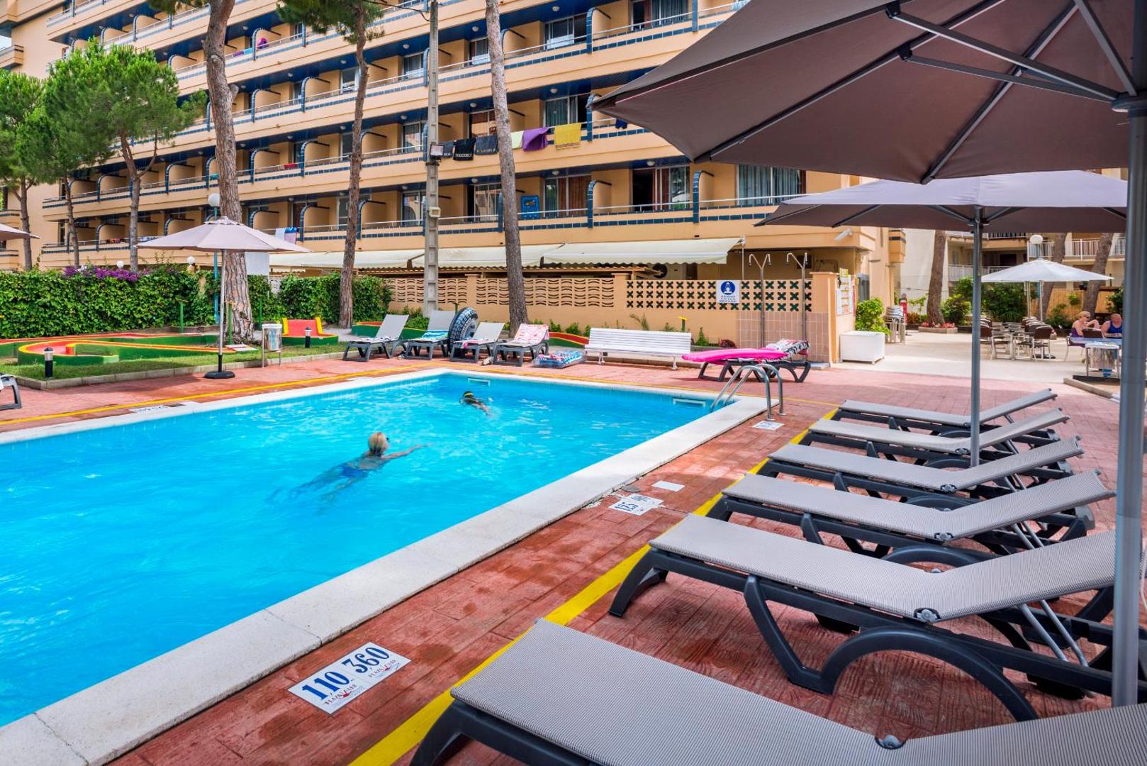 4R Playa Park viesnīcas āra baseins Salovā, Spānijā — atpūtas zona ar sauļošanās krēsliem, saulessargiem un skatu uz viesnīcas ēku.