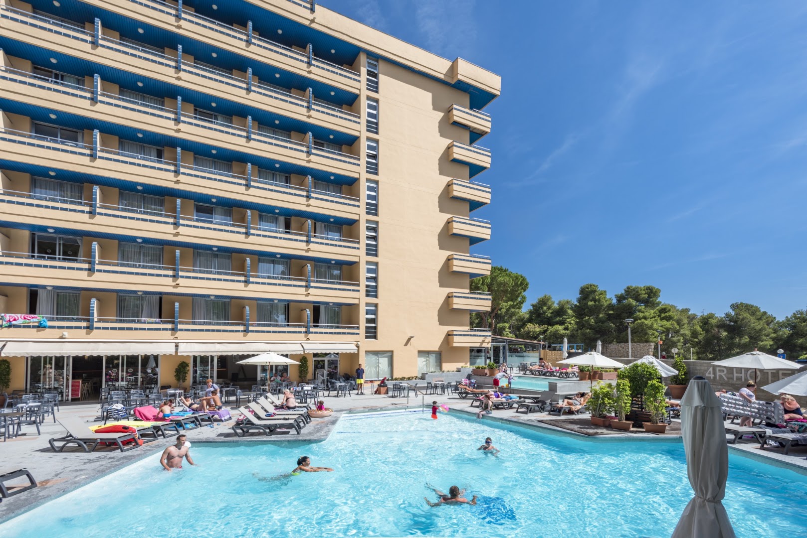 4R Playa Park āra baseins ar atpūtas krēsliem, saulessargiem un viesnīcas fasādi saulainā dienā Salovā.
