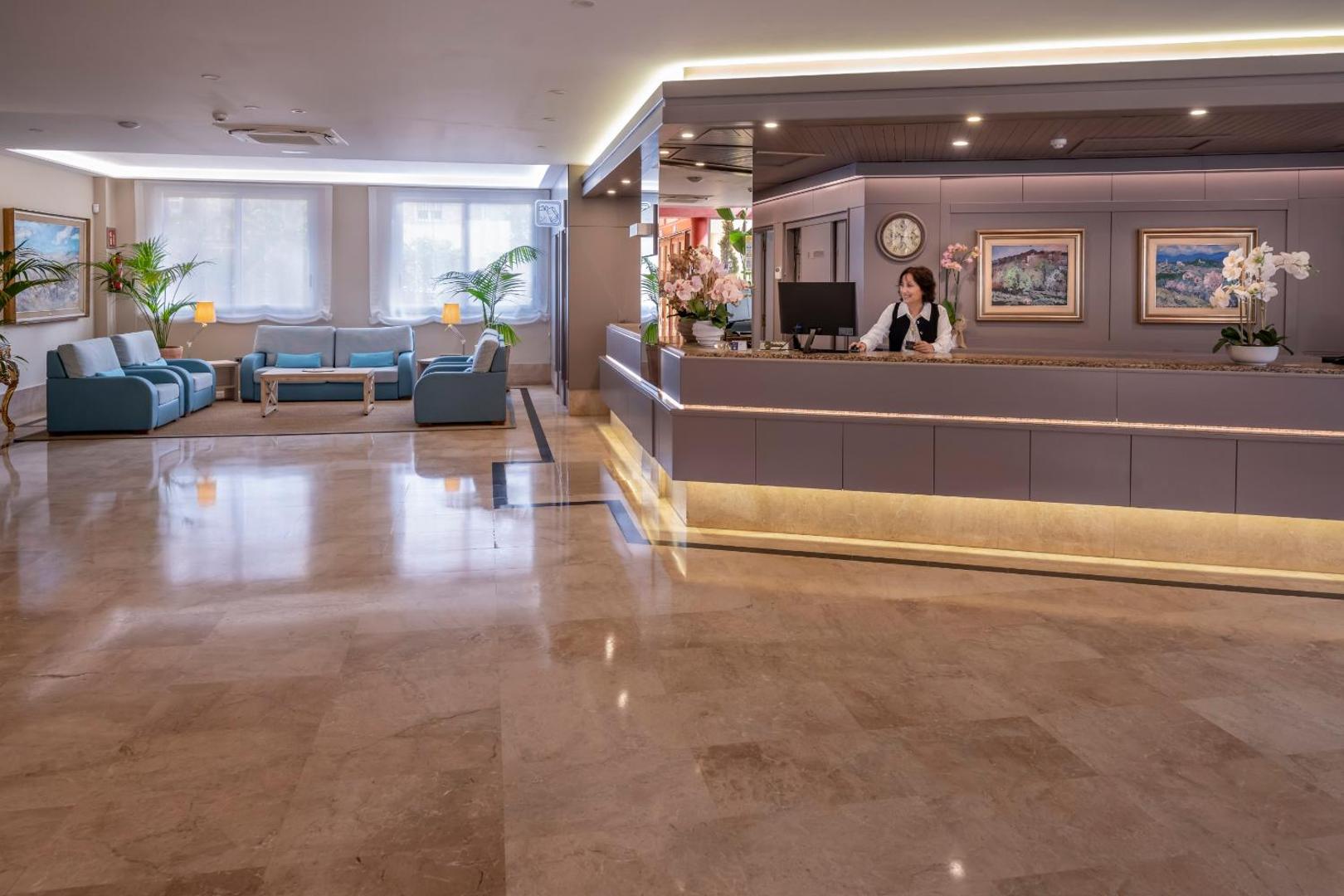 4R Playa Park viesnīcas recepcijas zona ar marmora grīdu, personālu un atpūtas stūrīti — plašs un gaišs vestibils viesu uzņemšanai.