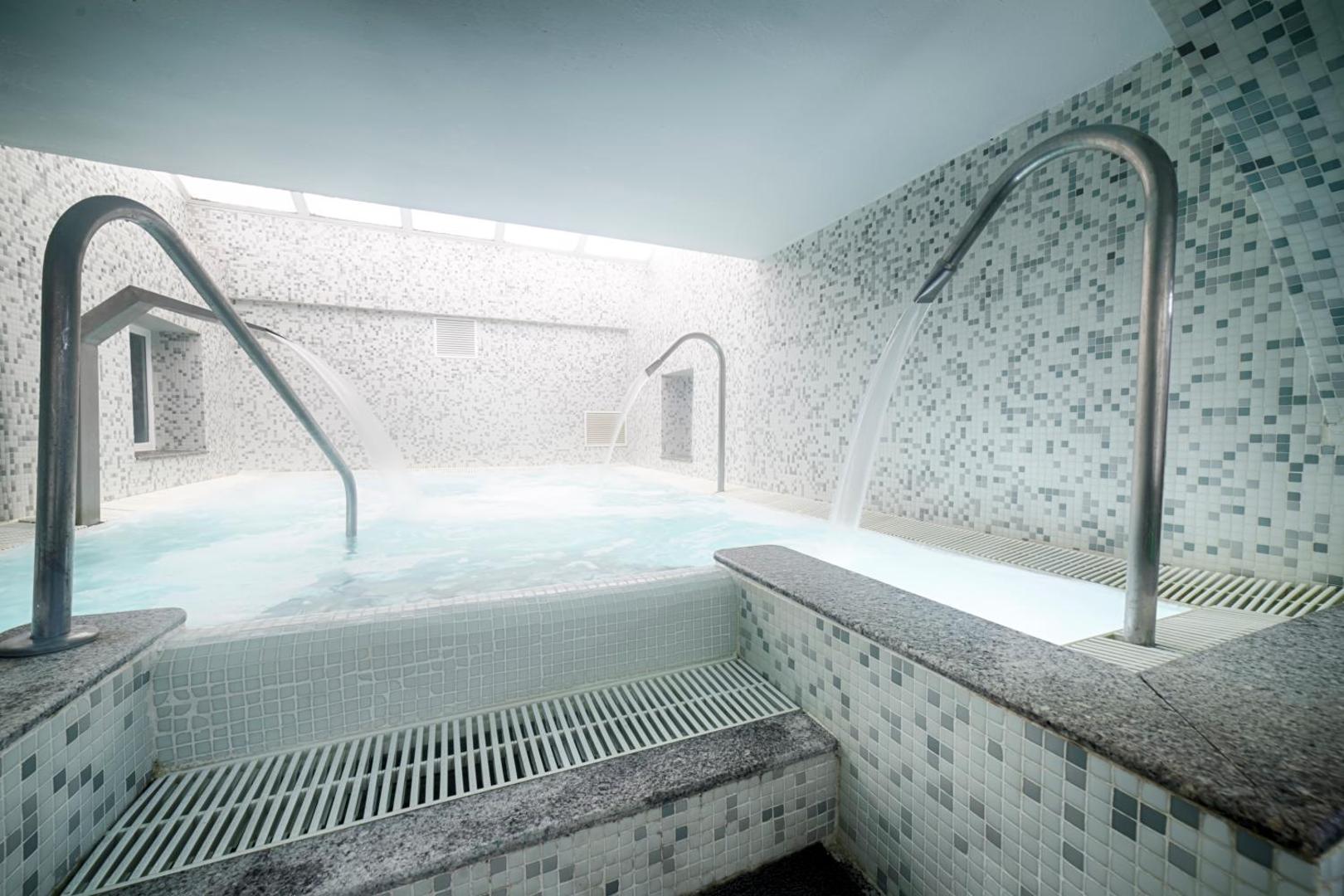 Viesnīcas Ohtels Belvedere spa centrs ar iekštelpu baseinu un vairākām ūdens kaskādēm relaksācijai, gaiša mozaīkas flīžu apdare