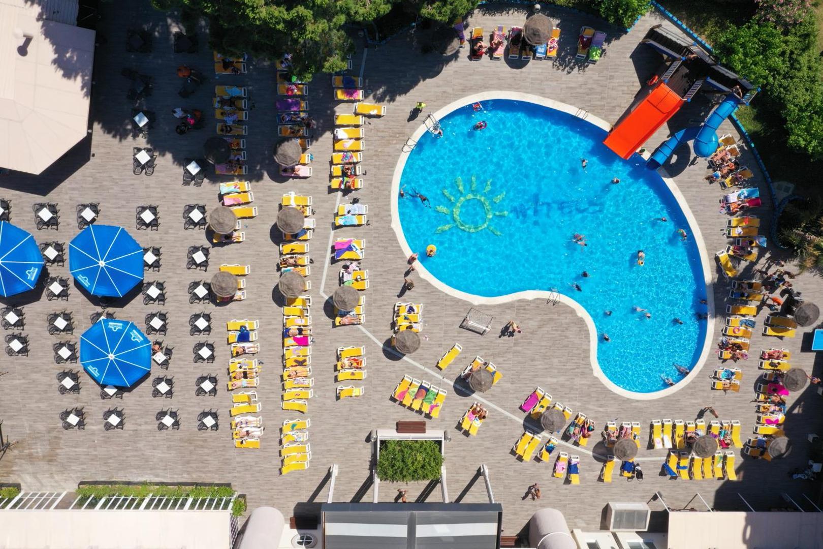 Ohtels Belvedere āra baseina zona no putna lidojuma Salovā — plaša sauļošanās terase ar krēsliem, saulessargiem un bērnu slidkalniņu