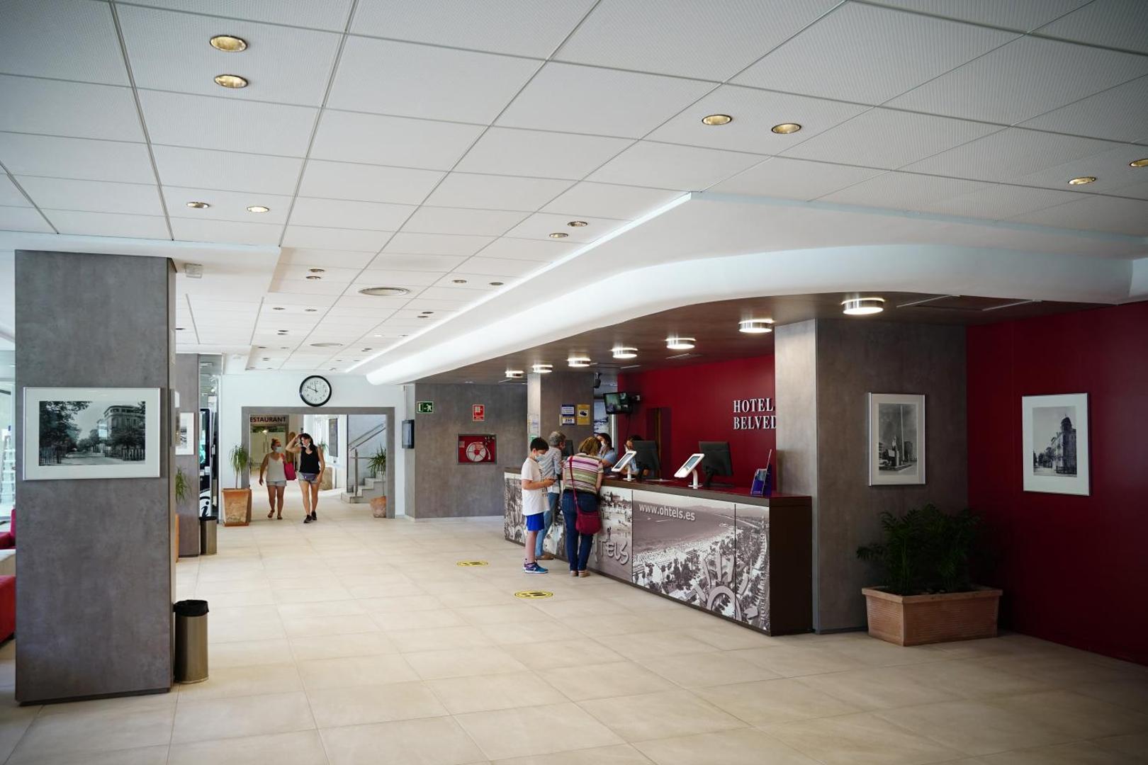 Ohtels Belvedere viesnīcas lobby zona un recepcijas lete Salovā — moderns interjers ar sarkanu akcenta sienu un informācijas stendu