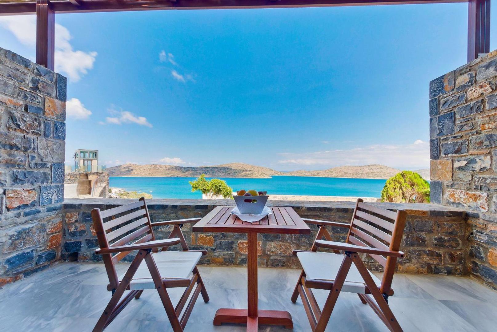 Royal Marmin Bay Boutique & Art Hotel numura terase ar koka mēbelēm un akmens sienām, skats uz zilo jūru Krētā