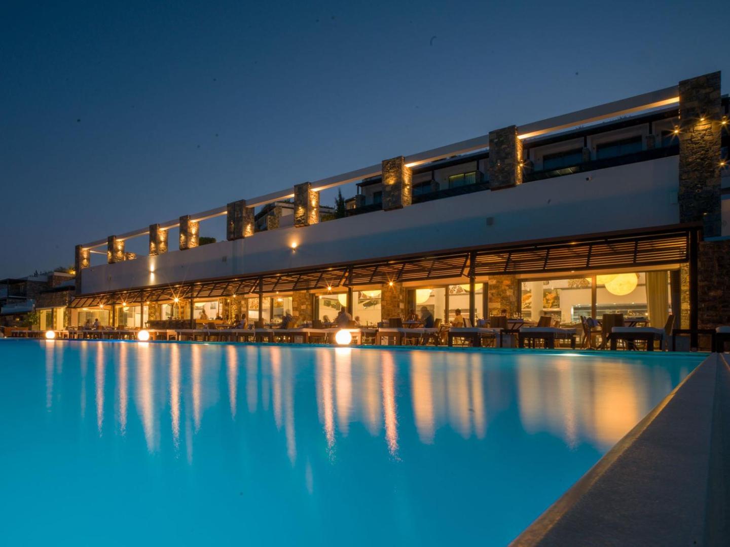 Royal Marmin Bay Boutique & Art Hotel izgaismots āra baseins vakarā Elundā, Krētā, ar skatu uz viesnīcas restorāna terasi