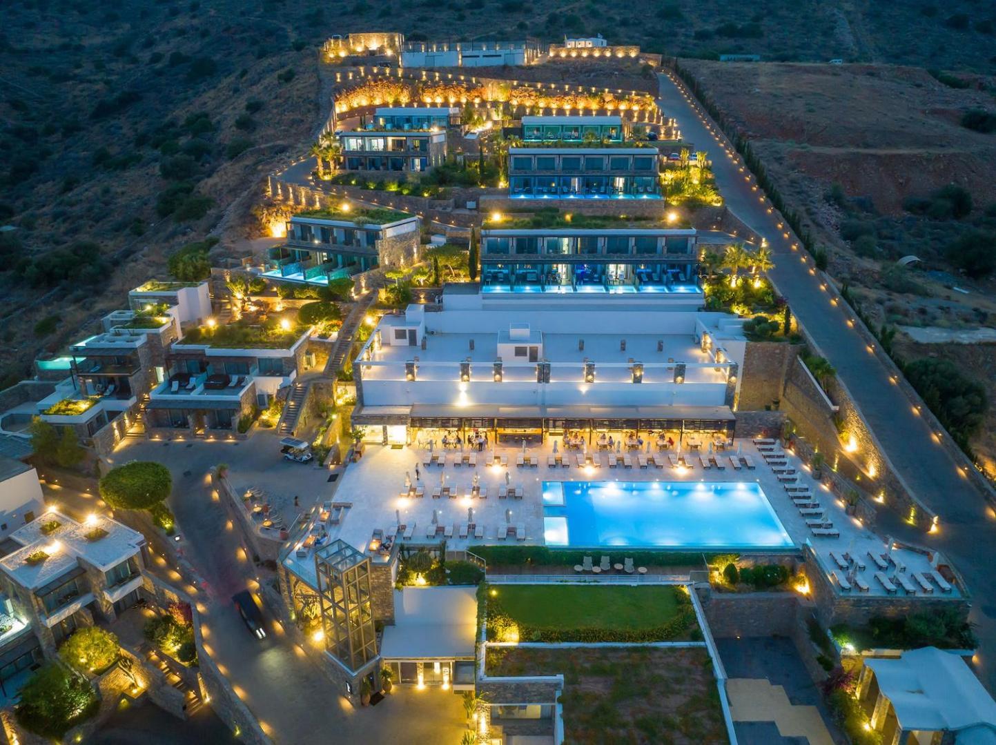 Royal Marmin Bay Boutique & Art Hotel teritorijas skats no augšas vakarā — galvenais baseins, terases un numuri ar privātiem baseiniem.