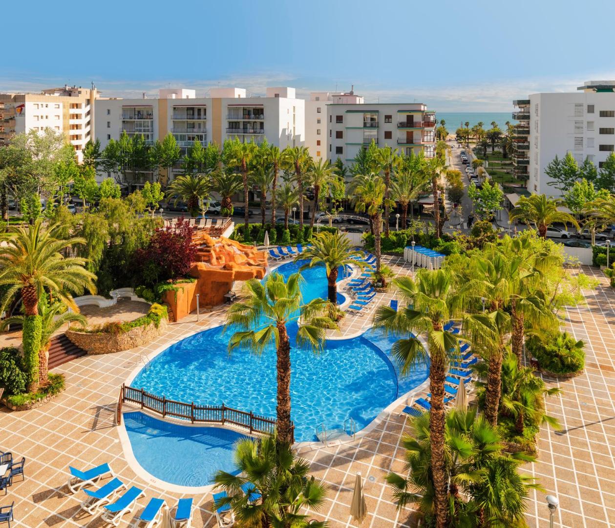 Skats no augšas uz H10 Salou Princess baseina zonu, palmām un apkārtējo pilsētas arhitektūru ar jūras horizontu tālumā