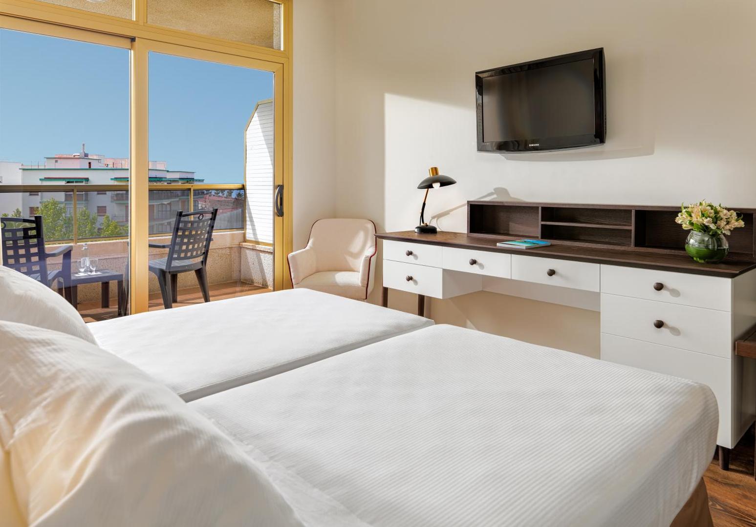 Moderns viesnīcas H10 Salou Princess numurs ar baltu rakstāmgaldu, televizoru un izeju uz mēbelētu balkonu Salovā
