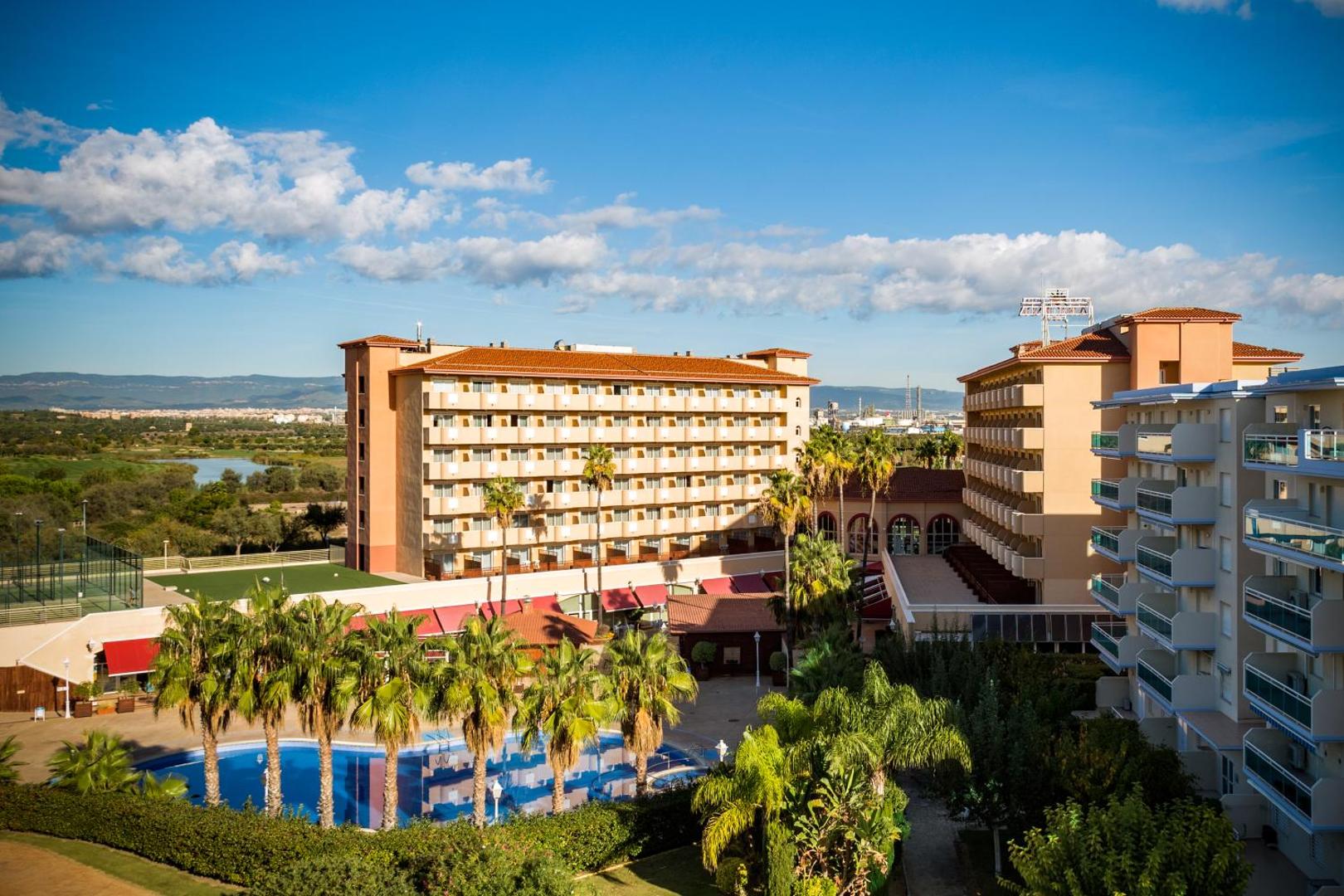 Panorāmas skats uz Ohtels La Hacienda kompleksu, baseinu un apkārtējo ainavu La Pinedas kūrortā pēcpusdienas saulē