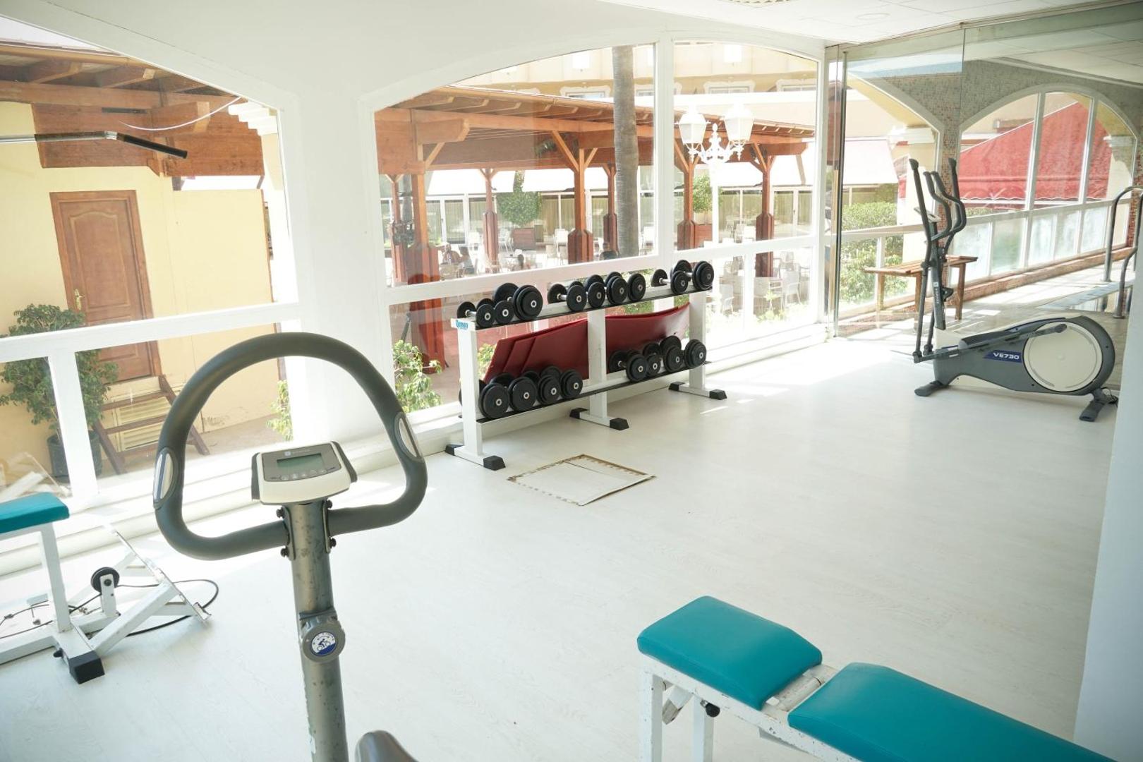 Gaiša Ohtels La Hacienda fitnesa zāle ar trenažieriem, hantelēm un skatu uz iekšpagalmu — sporta iespējas viesnīcas teritorijā