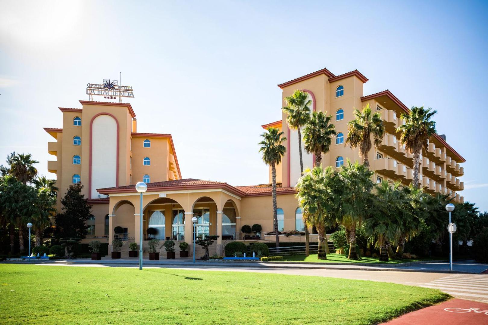 Viesnīcas Ohtels La Hacienda galvenā ieeja un fasāde dienas gaismā ar koptu zālienu un palmām Kosta Doradas reģionā