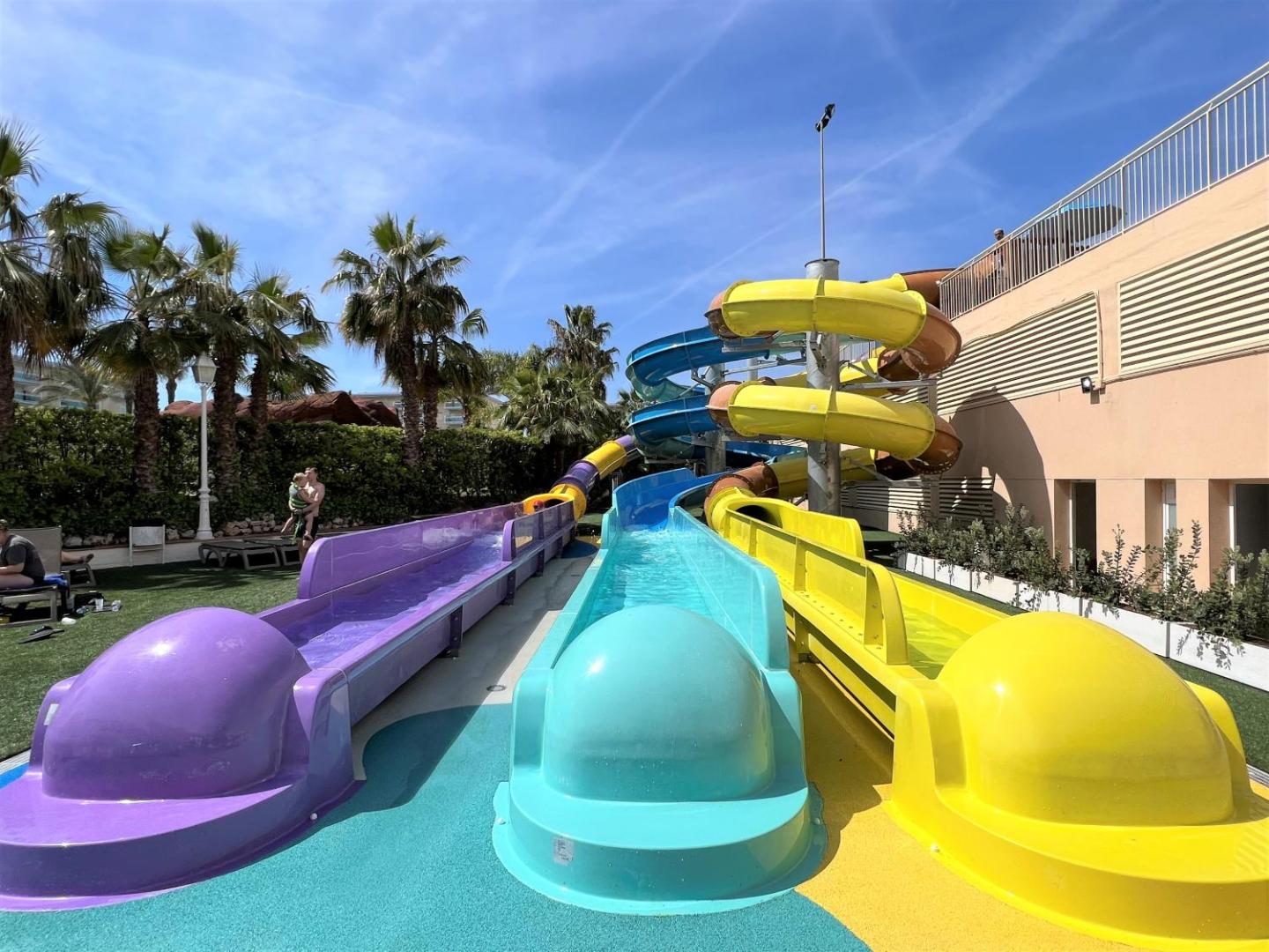Ohtels La Hacienda akvaparks ar vairākiem paralēliem ūdens slidkalniņiem un drošu zonu bērnu rotaļām saulainā laikā.