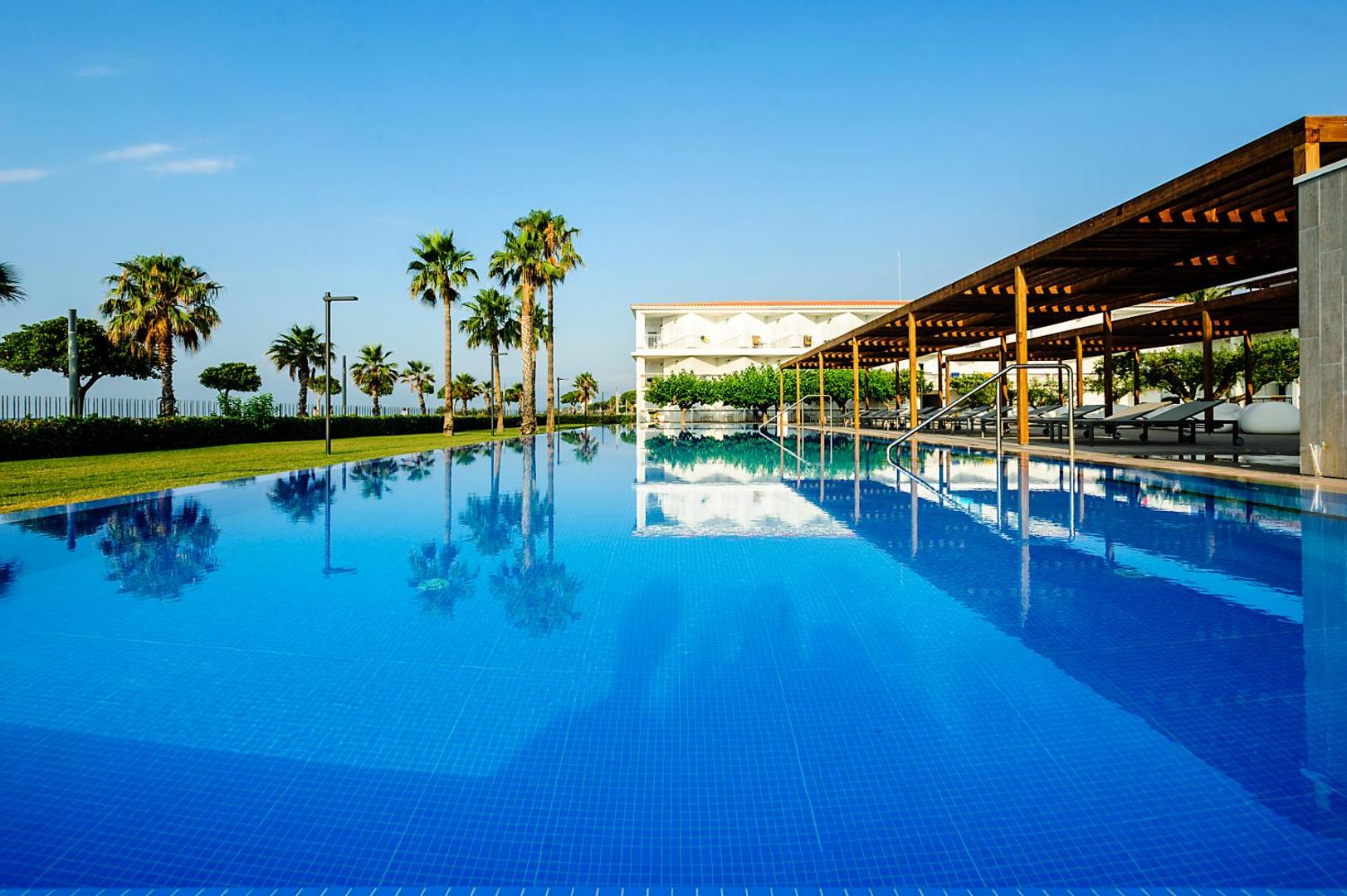 Estival Eldorado Resort lielais āra baseins ar pārplūdes malu, palmām un sauļošanās zonu zem koka nojumes Kostadoradā