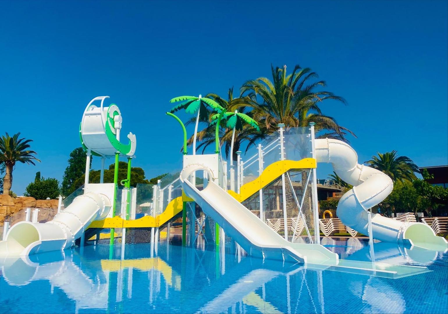 Estival Eldorado Resort bērnu ūdens atrakciju parks ar vairākiem slidkalniņiem un dekoratīvām palmām seklā baseinā zem skaidrām debesīm.