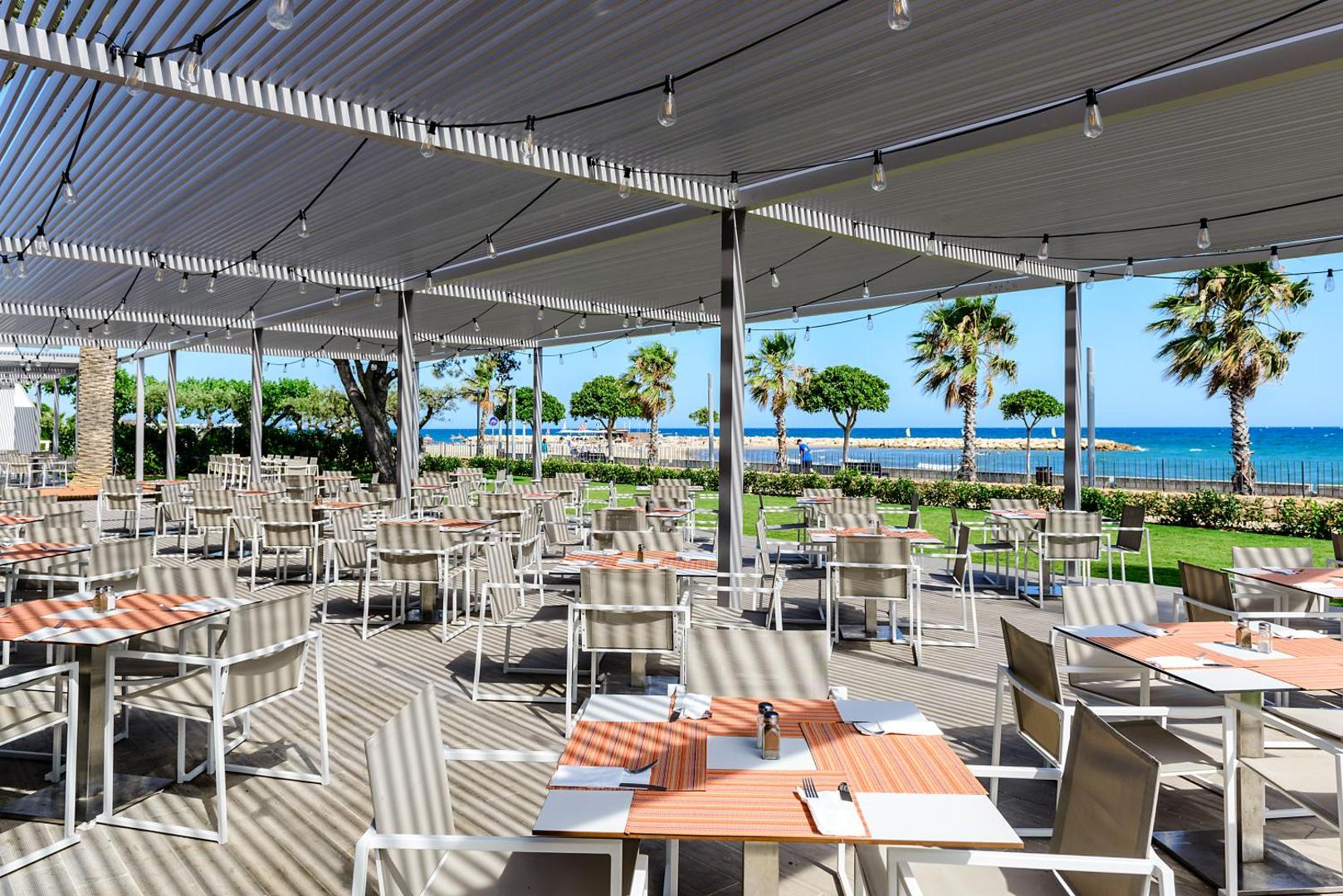 Estival Eldorado Resort plaša āra restorāna zona ar nojumi, daudziem galdiņiem un skatu uz piekrasti un palmām.