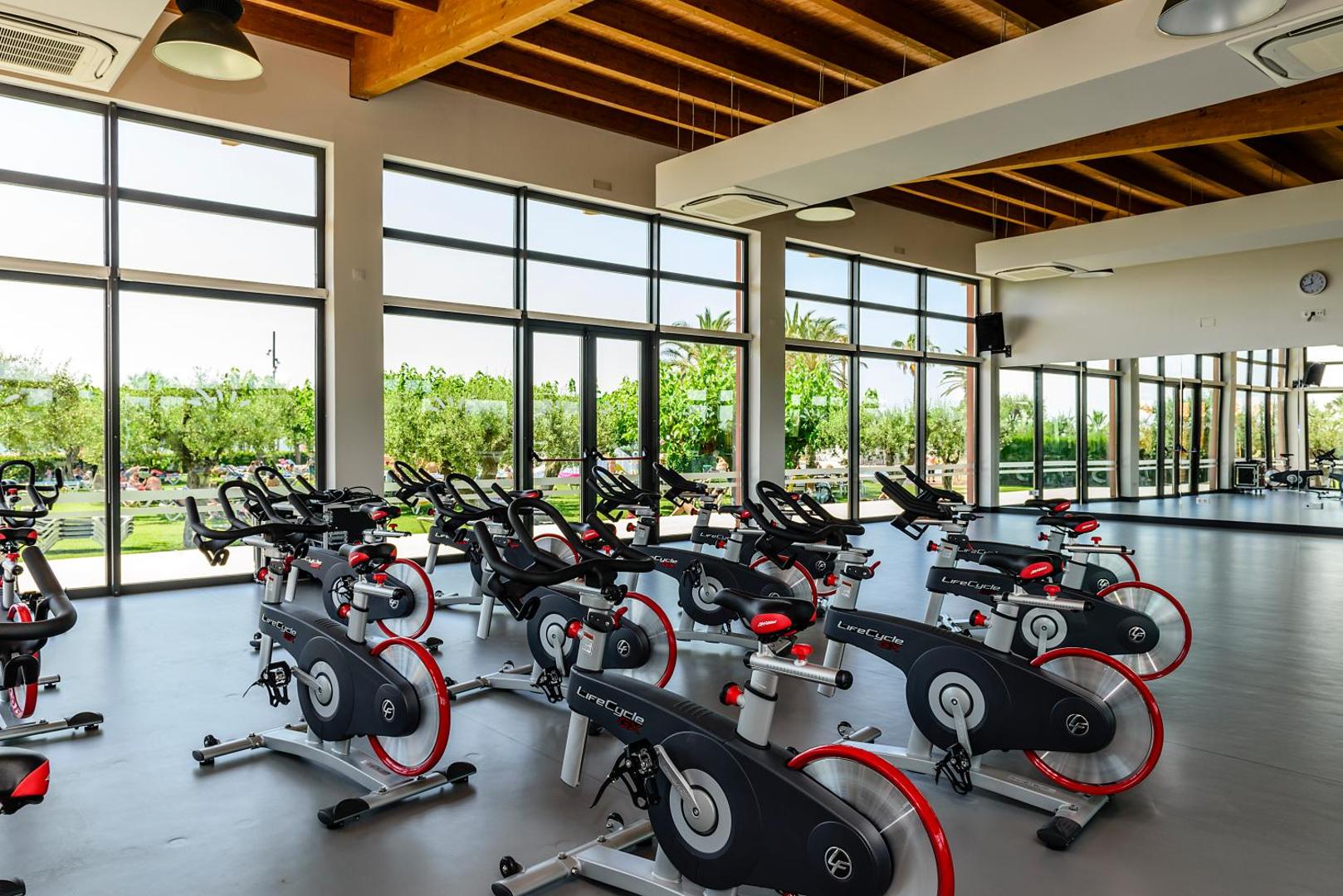 Estival Eldorado Resort velotrenažieru zāle ar skatu uz dārzu — profesionāls aprīkojums grupu nodarbībām un individuāliem treniņiem.