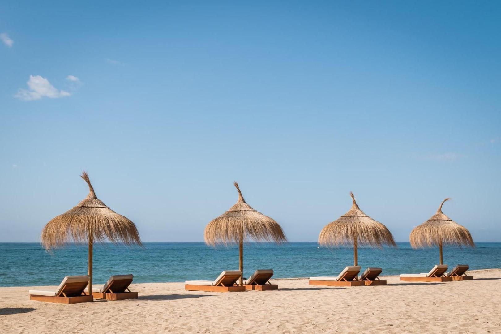 Estival Centurion Playa privātā pludmale ar salmu saulessargiem un koka sauļošanās gultām uz smilšu fona pie zilās jūras