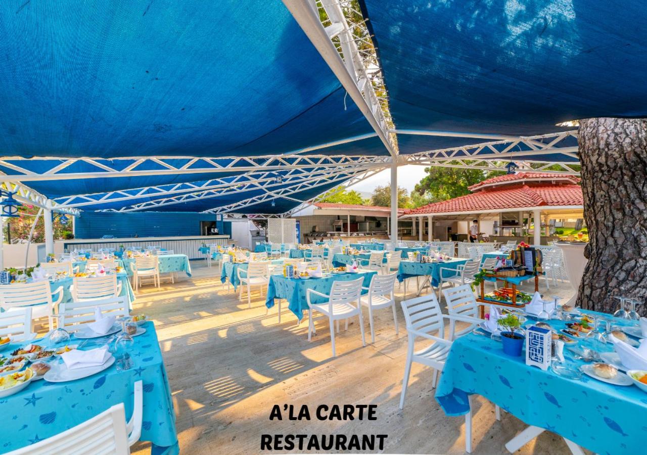 Kilikya Palace Goynuk a la carte restorāns zem zilas nojumes ar jūras tematikas galdautiem un servētiem galdiem dārzā
