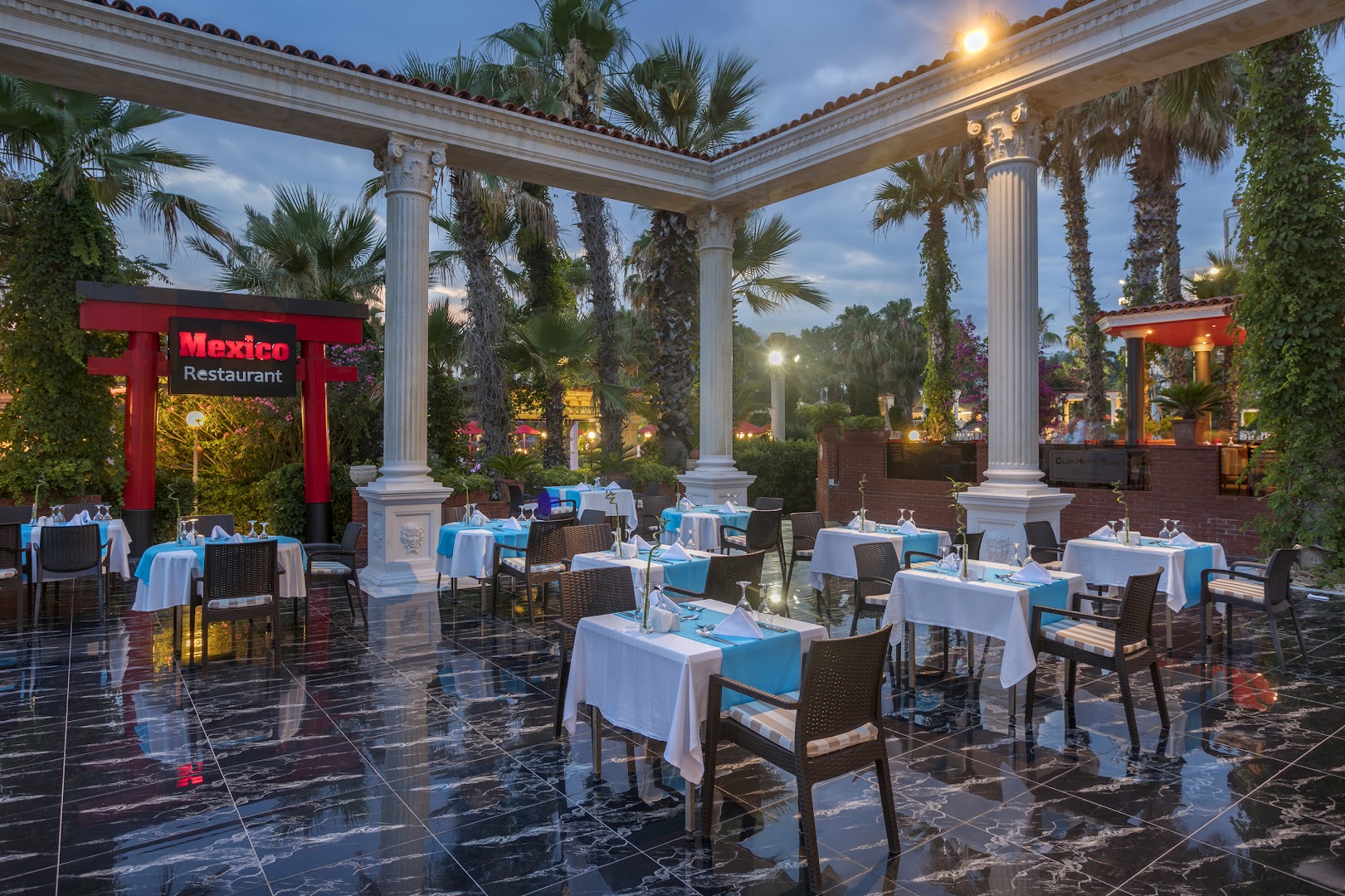 Club Hotel Sera Mexico restorāna āra terase vakarā ar balti klātiem galdiem un palmām Antalijas piekrastē