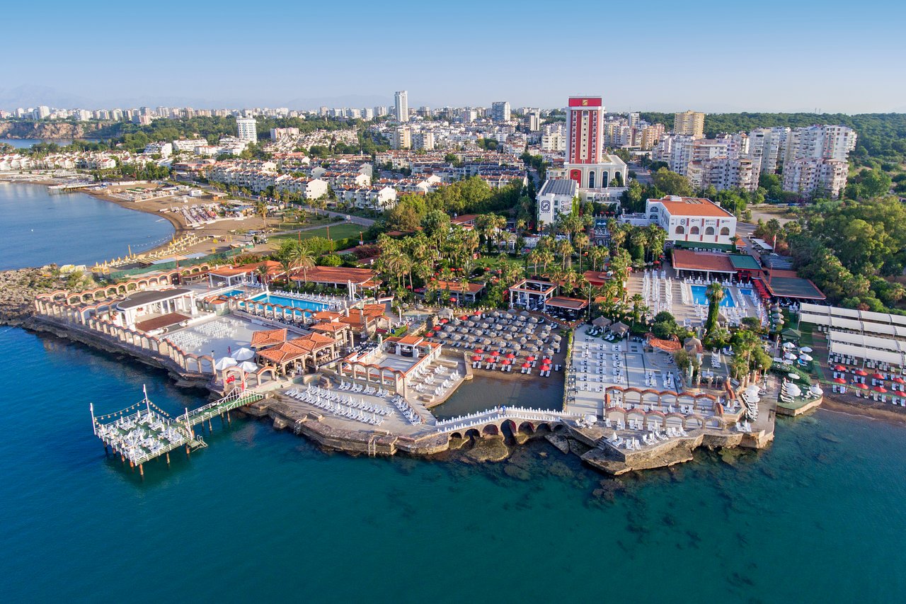 Club Hotel Sera panorāmas skats no putna lidojuma Antalijā — plaša teritorija pie Vidusjūras ar baseiniem, piestātni un pilsētas ainavu