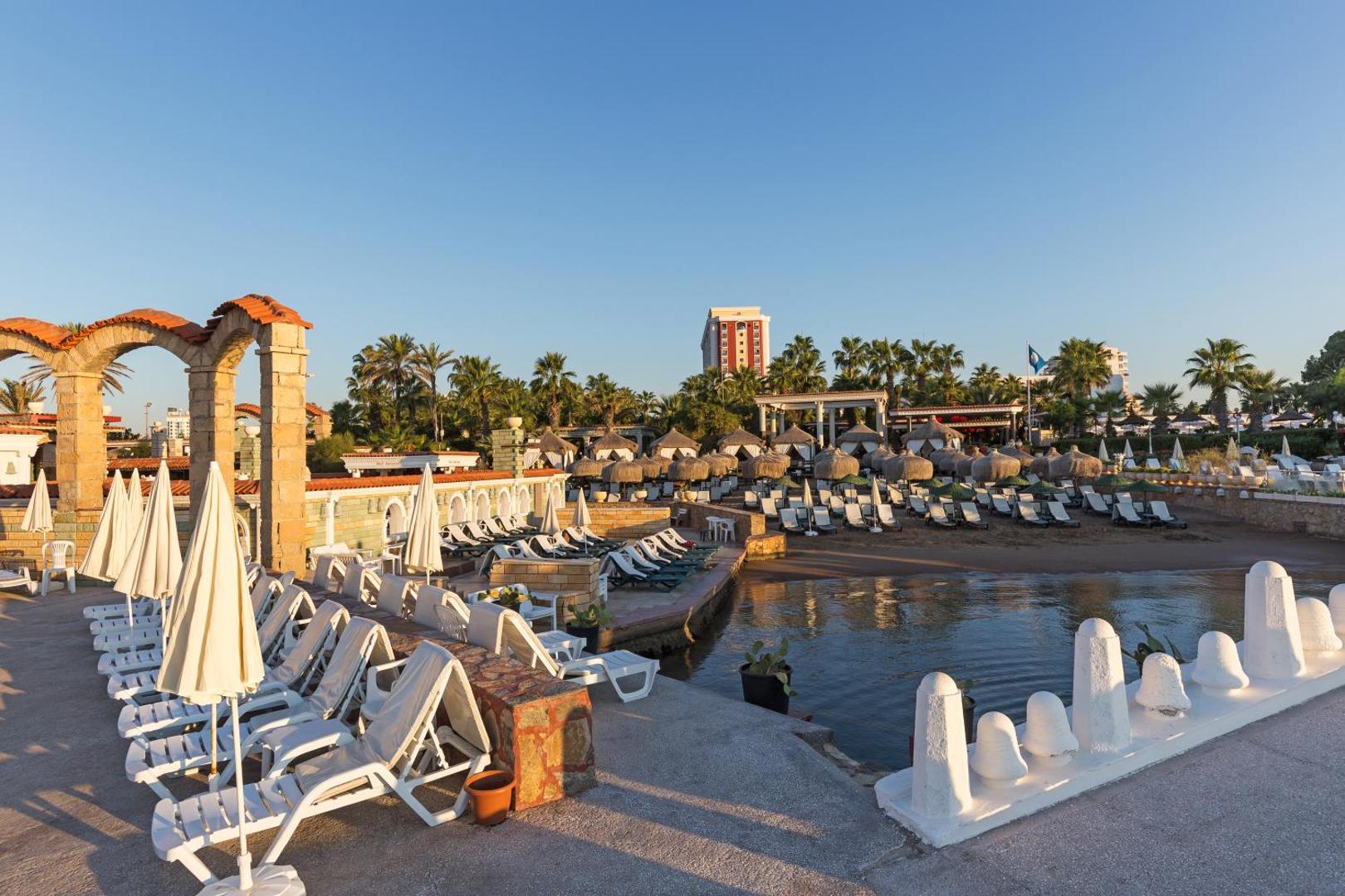 Club Hotel Sera pludmales zona ar sauļošanās krēsliem, saulessargiem un palmu dārzu Antalijā — skats uz viesnīcas teritoriju un baseinu