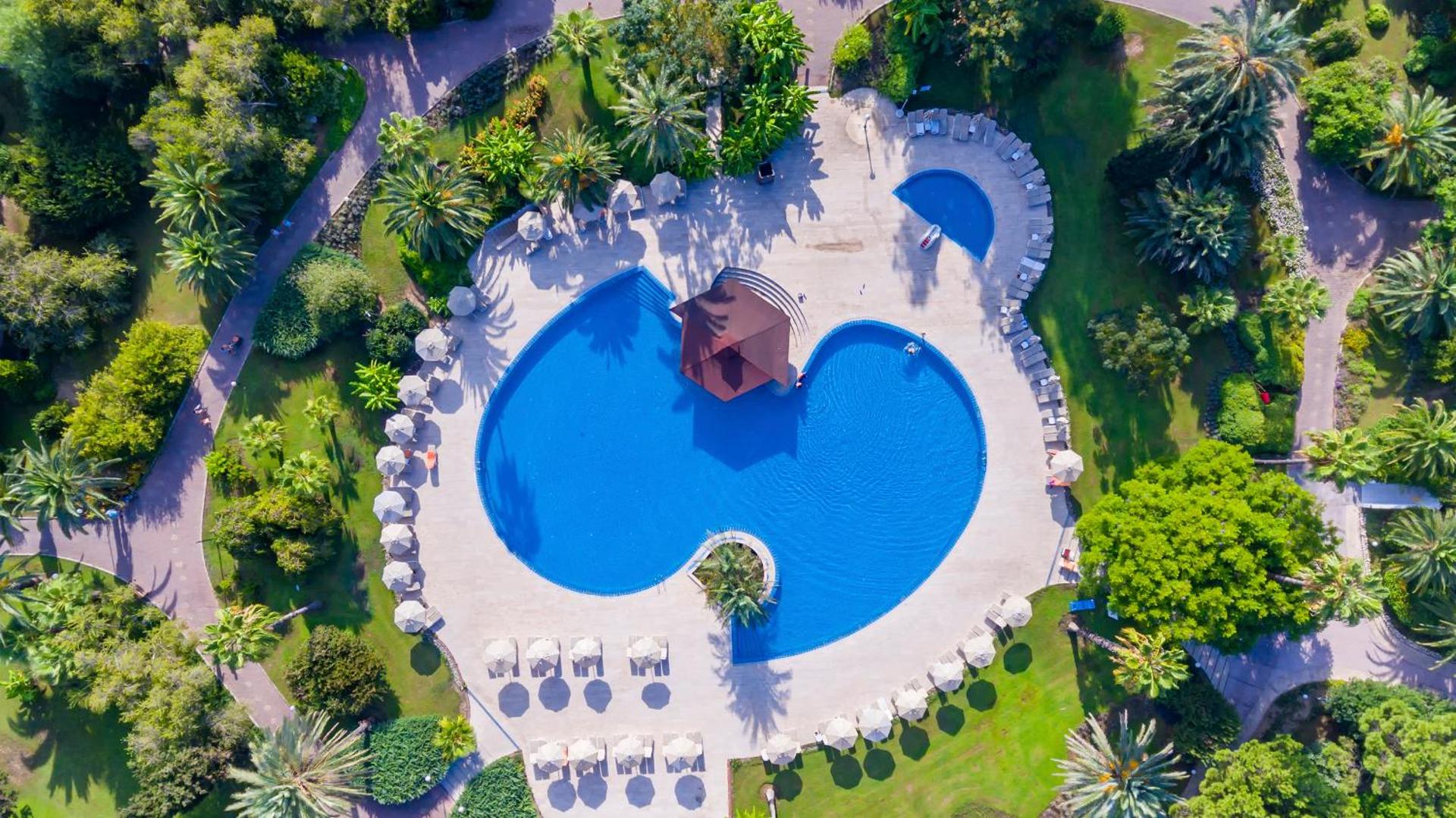 Starlight Resort dārza baseins no augšas ar bāru centrā, ko ieskauj palmas un sauļošanās krēsli