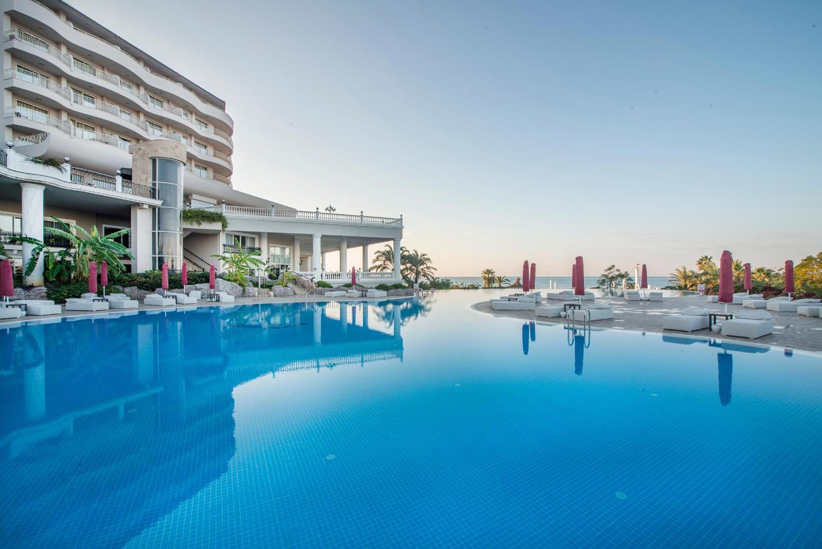 Starlight Resort viesnīcas ēka un bezmalas baseins saulrietā ar atpūtas krēsliem un saulessargiem piekrastē