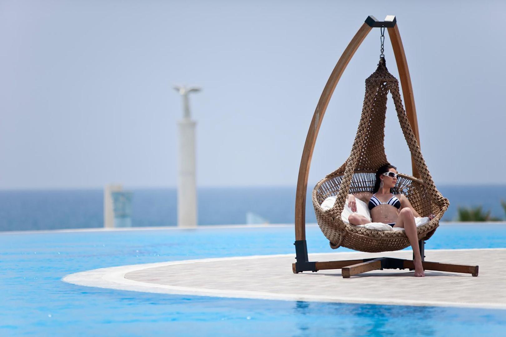 Starlight Resort atpūtas zona pie baseina ar piekārtu pīto krēslu, kurā atpūšas sieviete, fonā redzama jūra