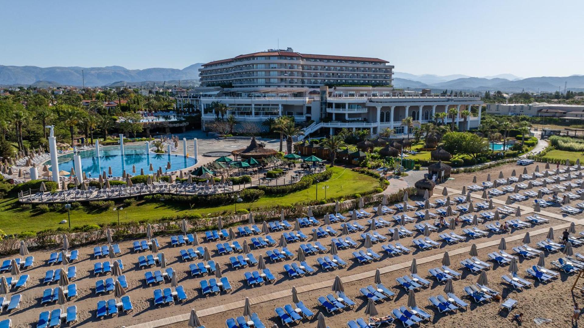 Skats uz Starlight Resort pludmales zonu ar daudziem sauļošanās krēsliem un viesnīcas ēku fonā saulainā dienā
