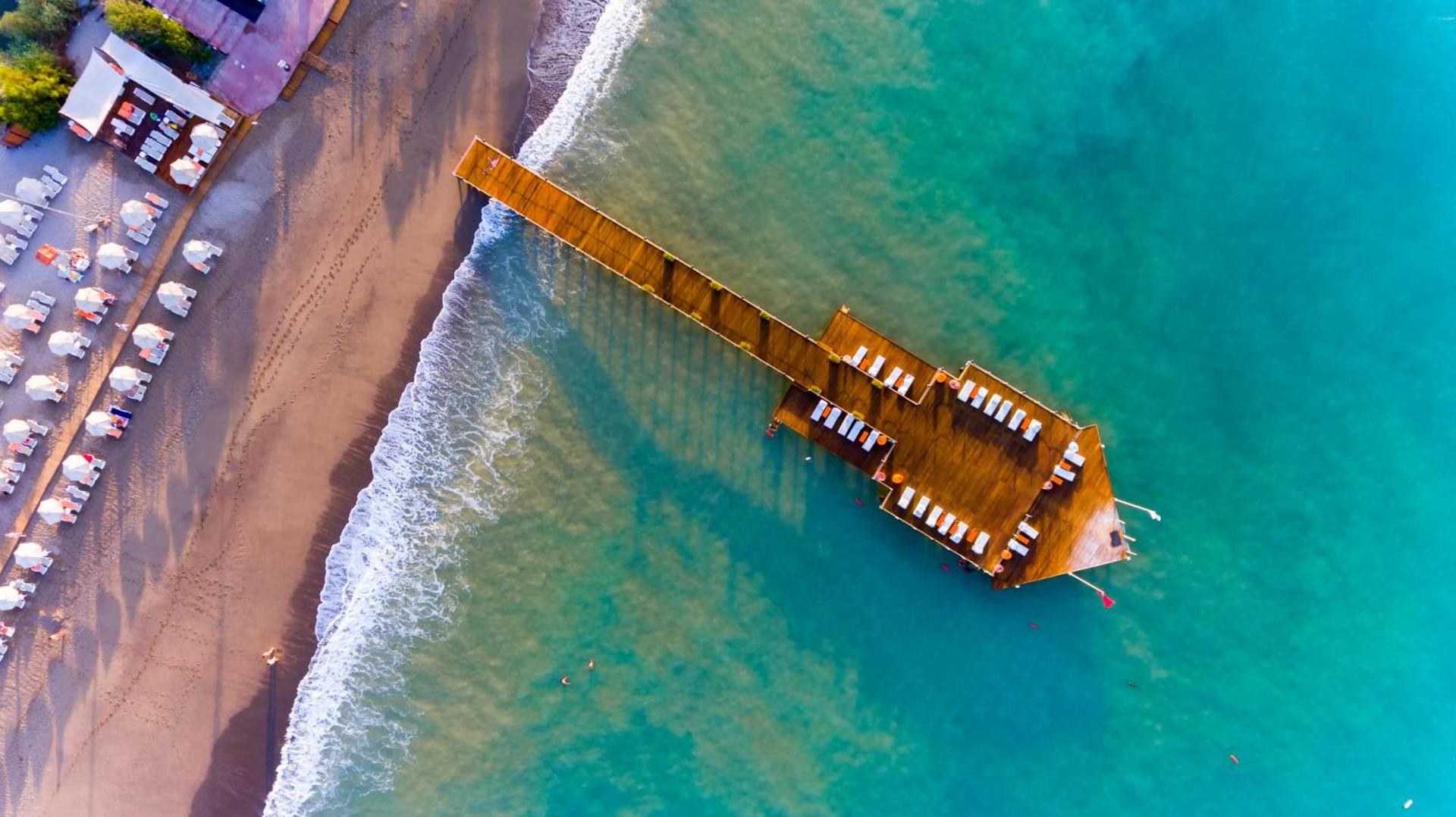 Starlight Resort koka mols no putna lidojuma Sidē — tirkīza krāsas ūdens, sauļošanās krēsli uz piestātnes un smilšu pludmale