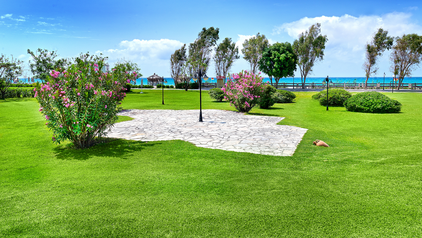Starlight Resort labiekārtota dārza teritorija ar koptu zālienu, ziedošiem krūmiem un skatu uz Vidusjūras piekrasti