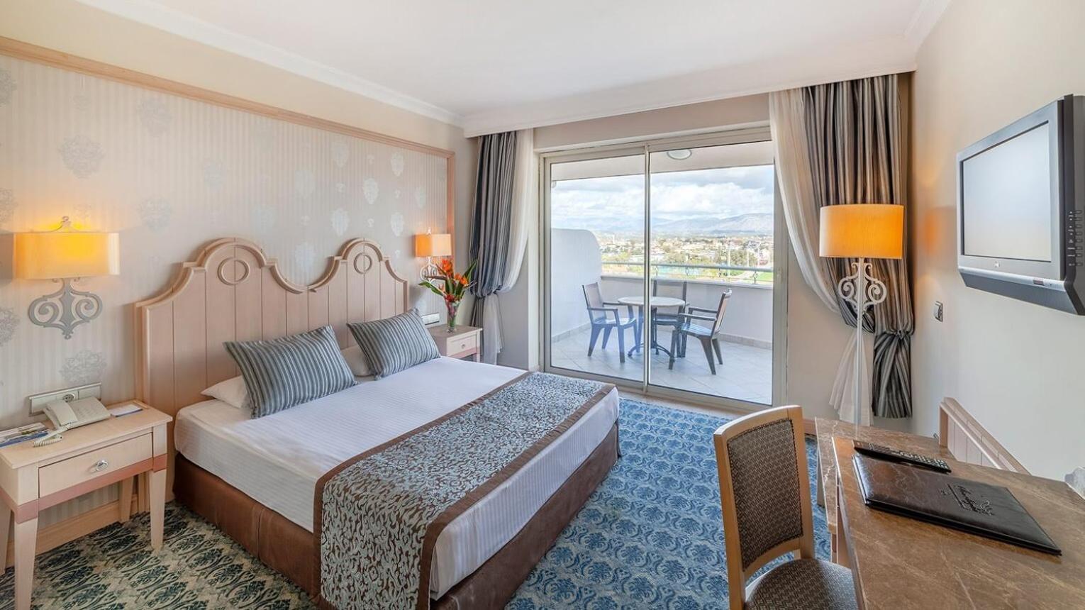Gaišs Starlight Resort viesnīcas numurs ar divguļamo gultu, rakstāmgaldu un balkonu, no kura paveras skats uz pilsētu un kalniem