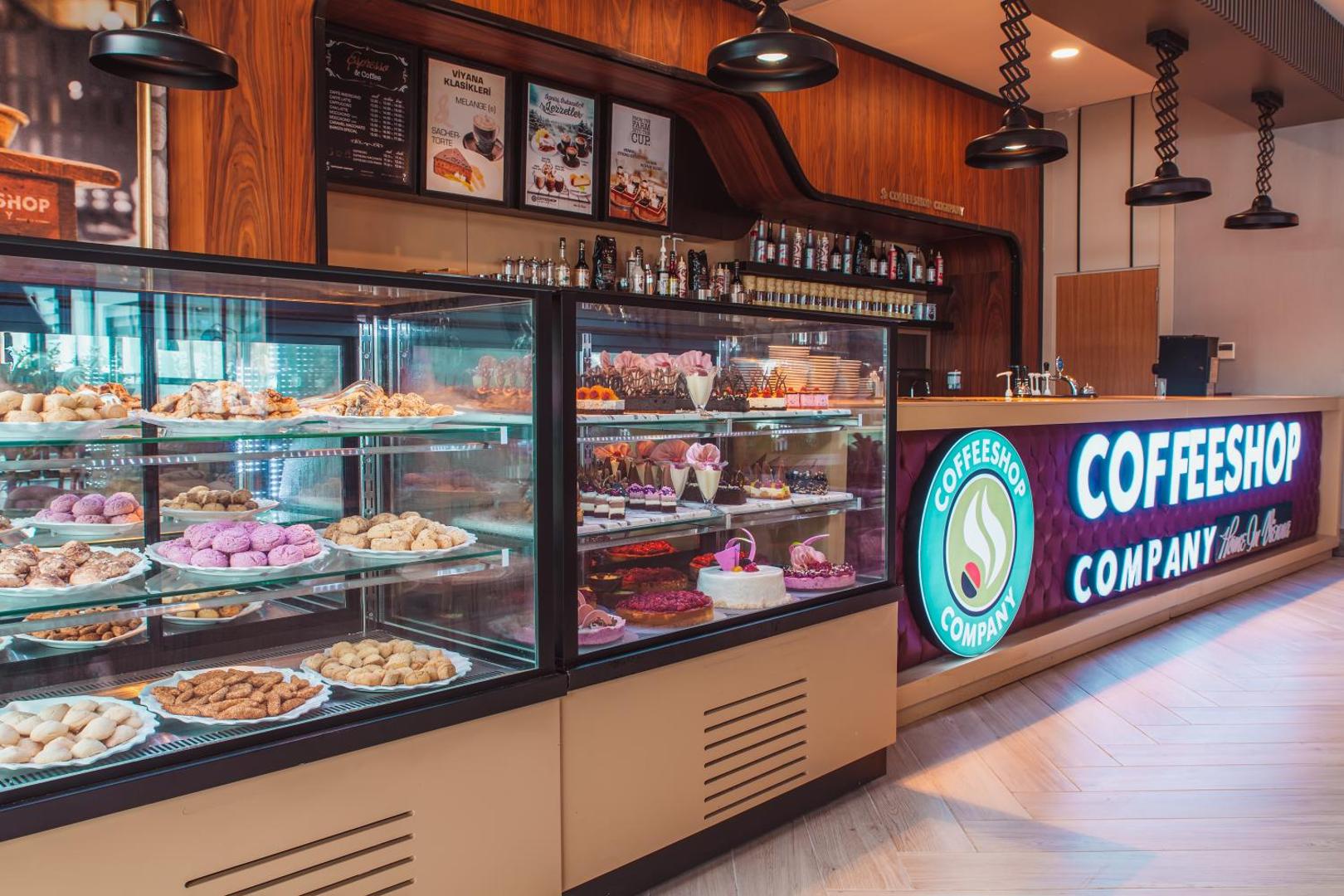 Side Royal Palace kafejnīca Coffeeshop Company ar plašu kūku, cepumu un desertu izvēli stikla vitrīnās