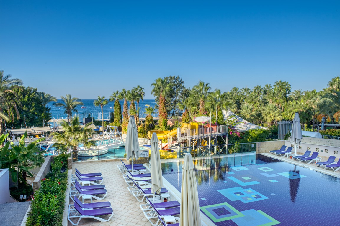Skats no augšas uz Sealife Buket Resort & Beach baseinu ar sauļošanās krēsliem, saulessargiem un palmu dārzu pie jūras.