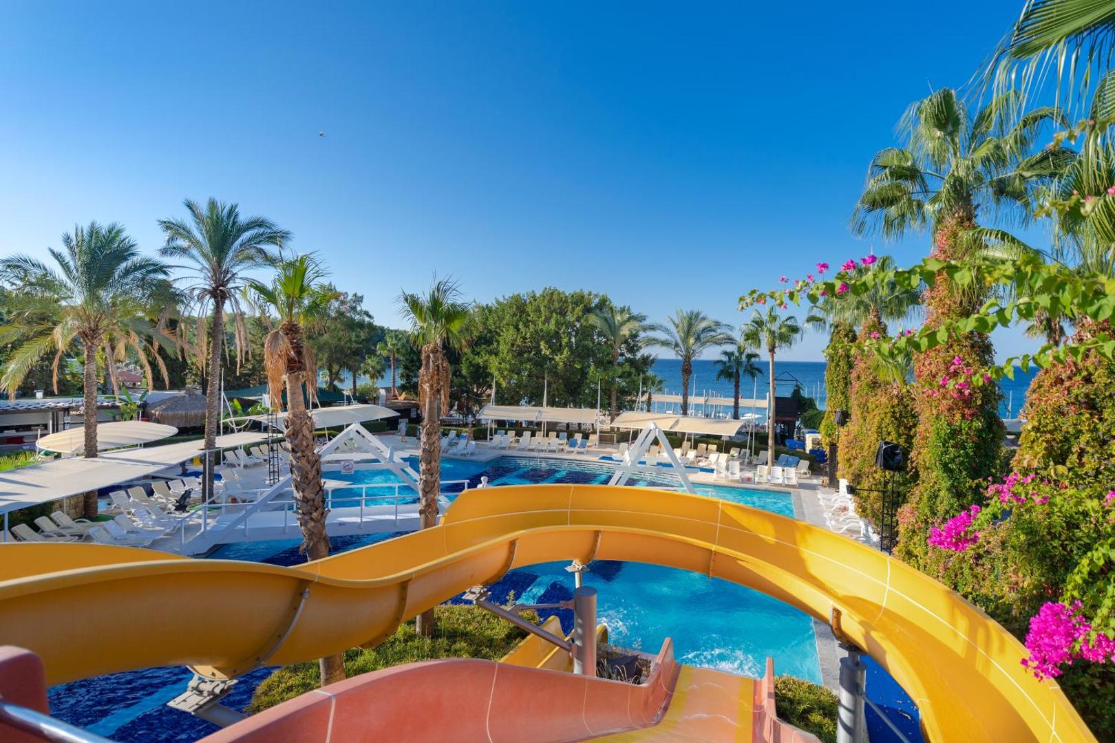 Sealife Buket Resort & Beach ūdens slidkalniņš ar skatu uz baseinu, palmām un zilo jūru fonā saulainā dienā.