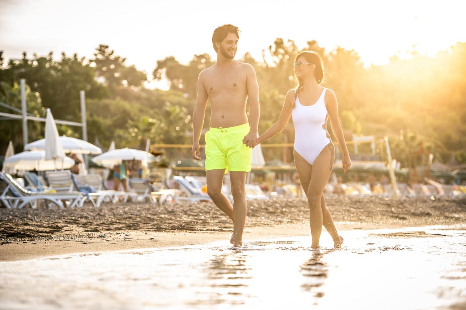 Pāris pastaigājas pa Sealife Buket Resort & Beach smilšu pludmali saules staros pie Vidusjūras krasta