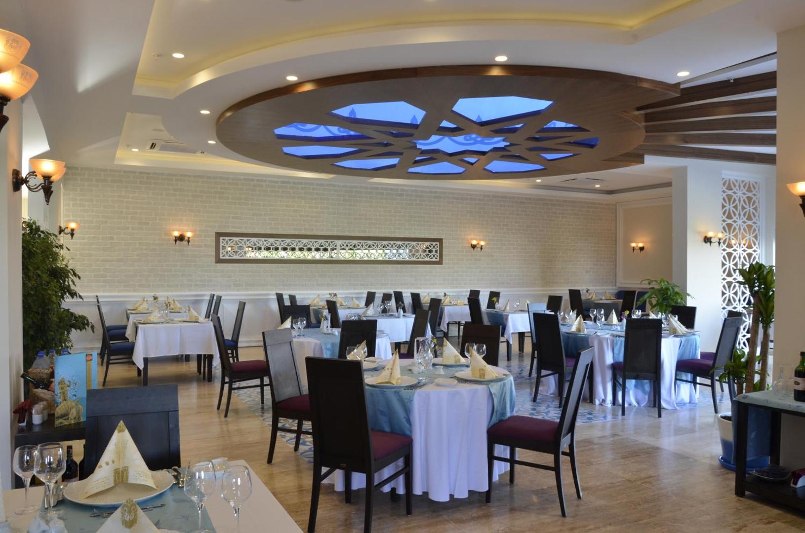Gaišs Emelda Sun Club restorāns ar eleganti klātiem galdiem, ziliem akcentiem un dekoratīvu griestu elementu