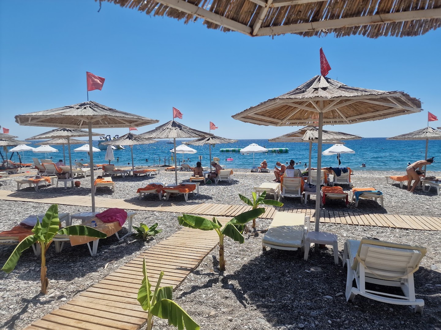 Emelda Sun Club oļu pludmale ar koka laipām, saulessargiem un zviļņiem saulainā dienā Kemerā