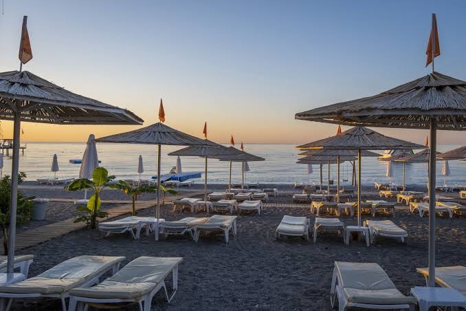 Emelda Sun Club pludmale saulrieta laikā ar salmu saulessargiem un zviļņiem Vidusjūras piekrastē Kemerā