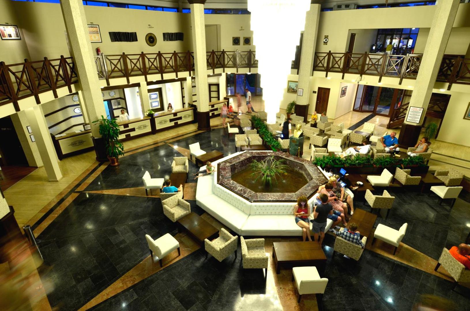 Emelda Sun Club viesnīcas lobby halle ar strūklaku centrā, atpūtas krēsliem un recepcijas zonu