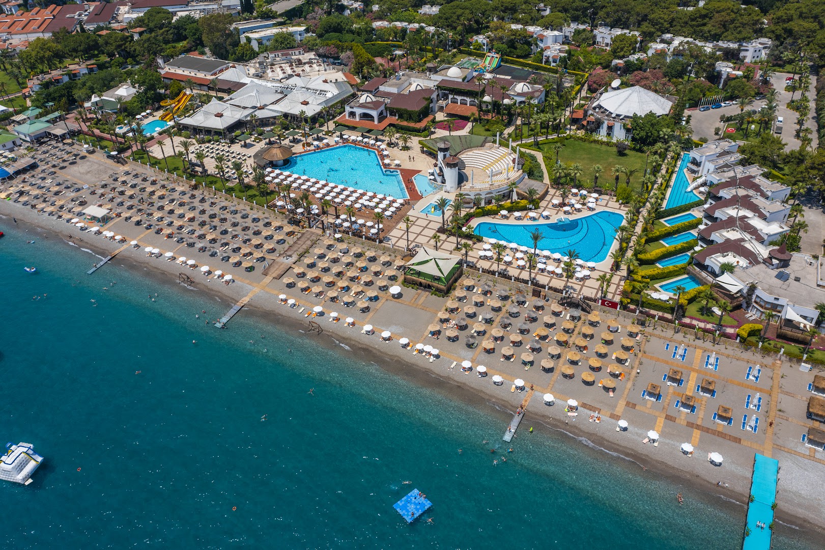 Emelda Sun Club plašā teritorija ar vairākiem baseiniem, amfiteātri un saulessargu zonu pie oļu pludmales