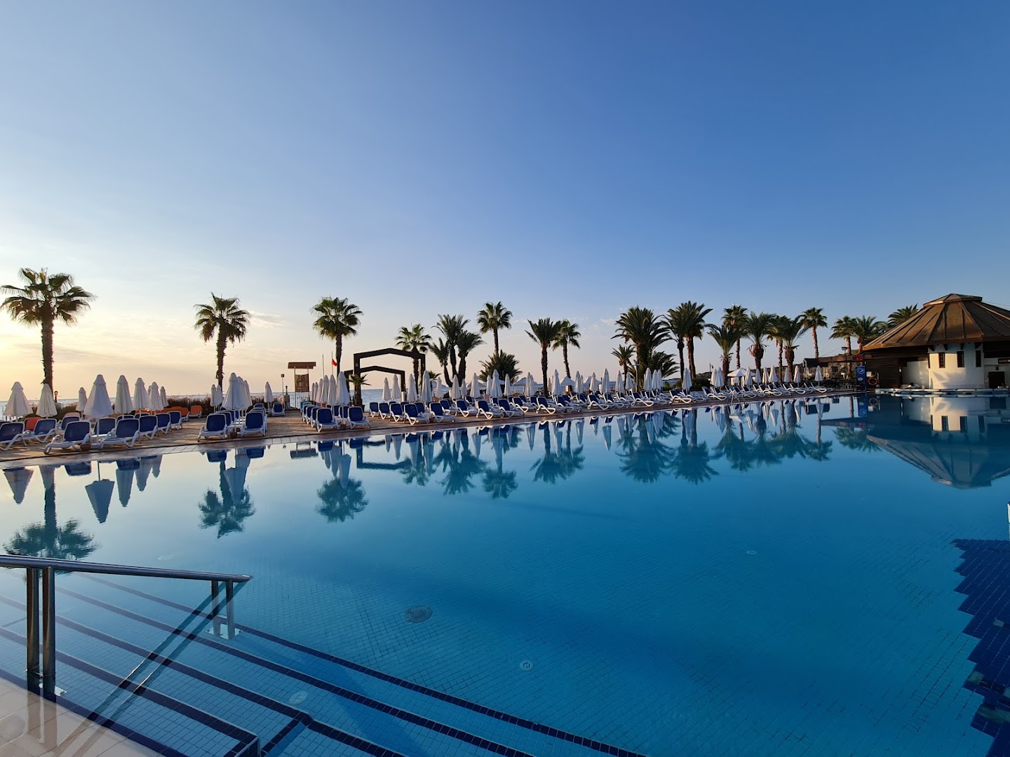 Emelda Sun Club plašais baseins ar palmām un saulessargiem rīta gaismā — skats uz Vidusjūras piekrasti Kemeras reģionā