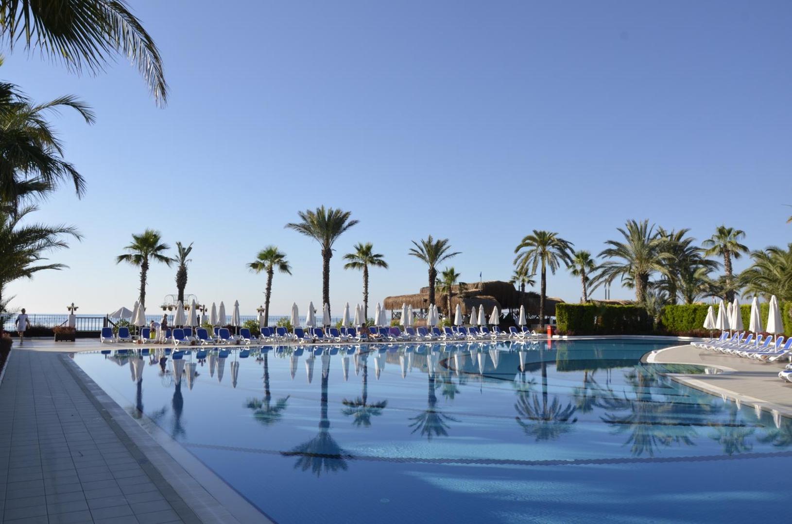 Emelda Sun Club baseina zona ar palmām un atpūtas krēsliem pie jūras Kemeras reģionā, Turcijā