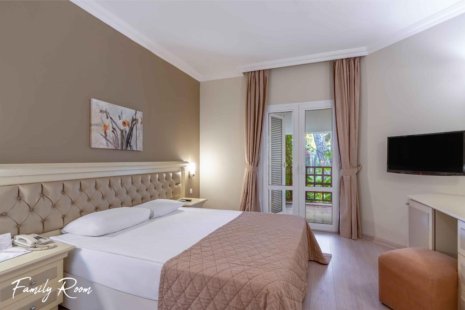 Emelda Sun Club ģimenes numurs ar plašu divguļamo gultu, gaišu interjeru un izeju uz balkonu dārza pusē