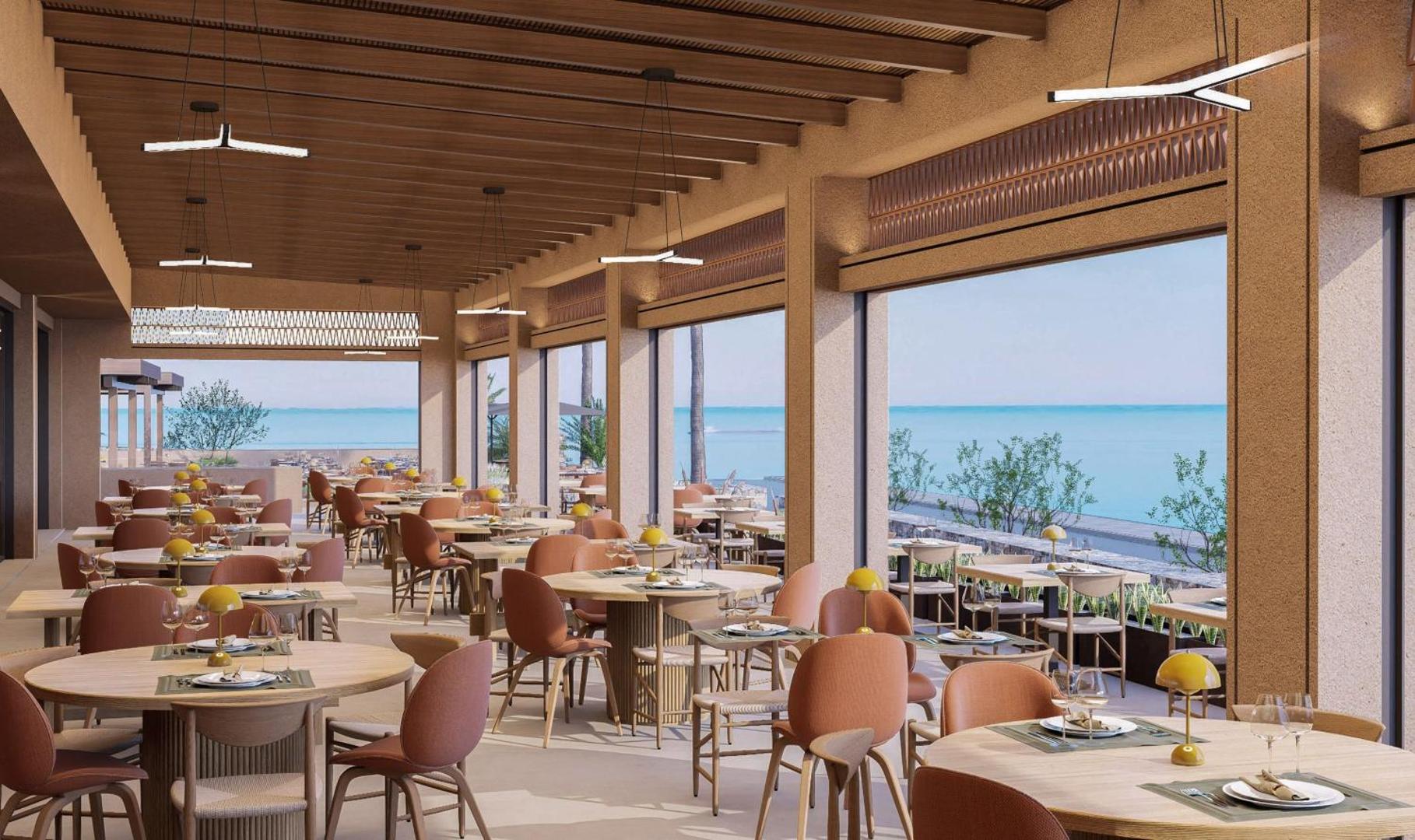 Blue Sea Beach viesnīcas restorāna iekštelpas ar lieliem panorāmas logiem, modernu dizainu un skatu uz piekrasti