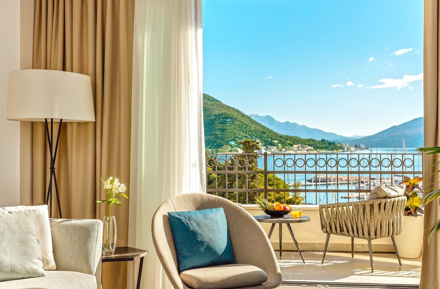 Skats no Lazure Hotel & Marina balkona uz Kotoras līča kalniem un jahtu piestātni saulainā dienā Melnkalnē