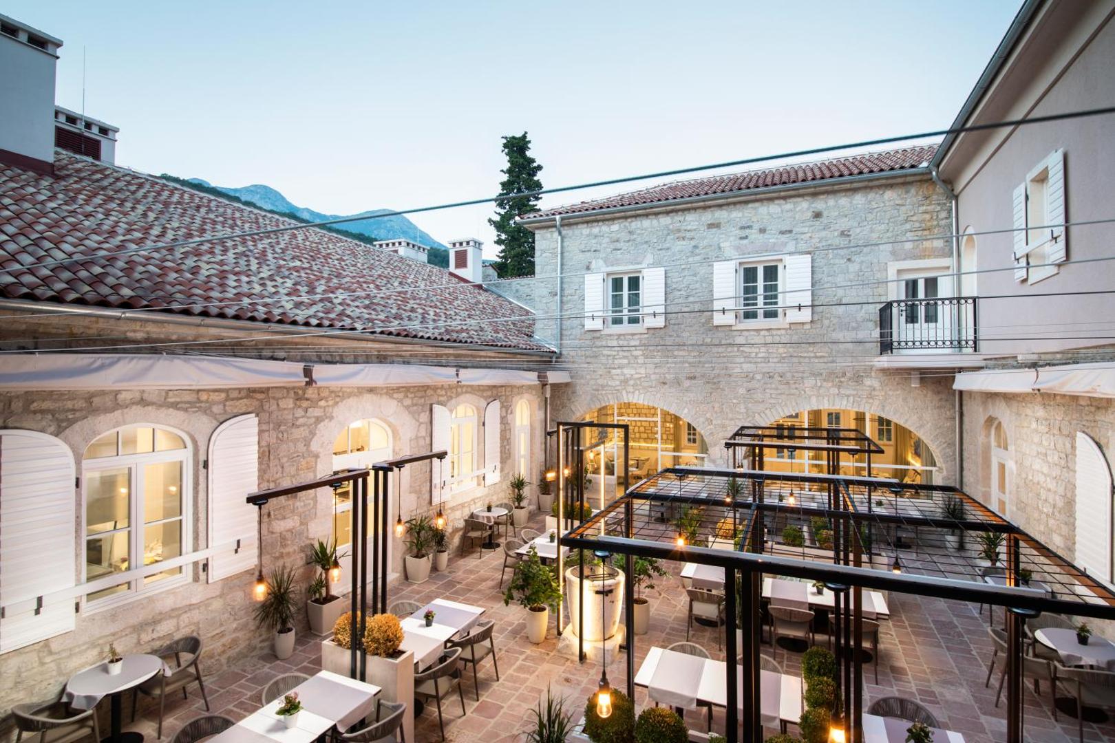Lazure Hotel & Marina izgaismots iekšpagalms vakarā ar restorāna zonu un skatu uz kalniem fonā