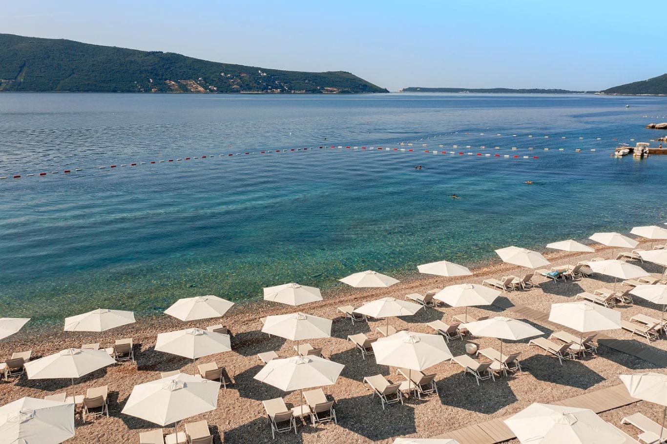 Lazure Hotel & Marina privātā oļu pludmale ar baltiem saulessargiem un sauļošanās krēsliem pie dzidra jūras ūdens