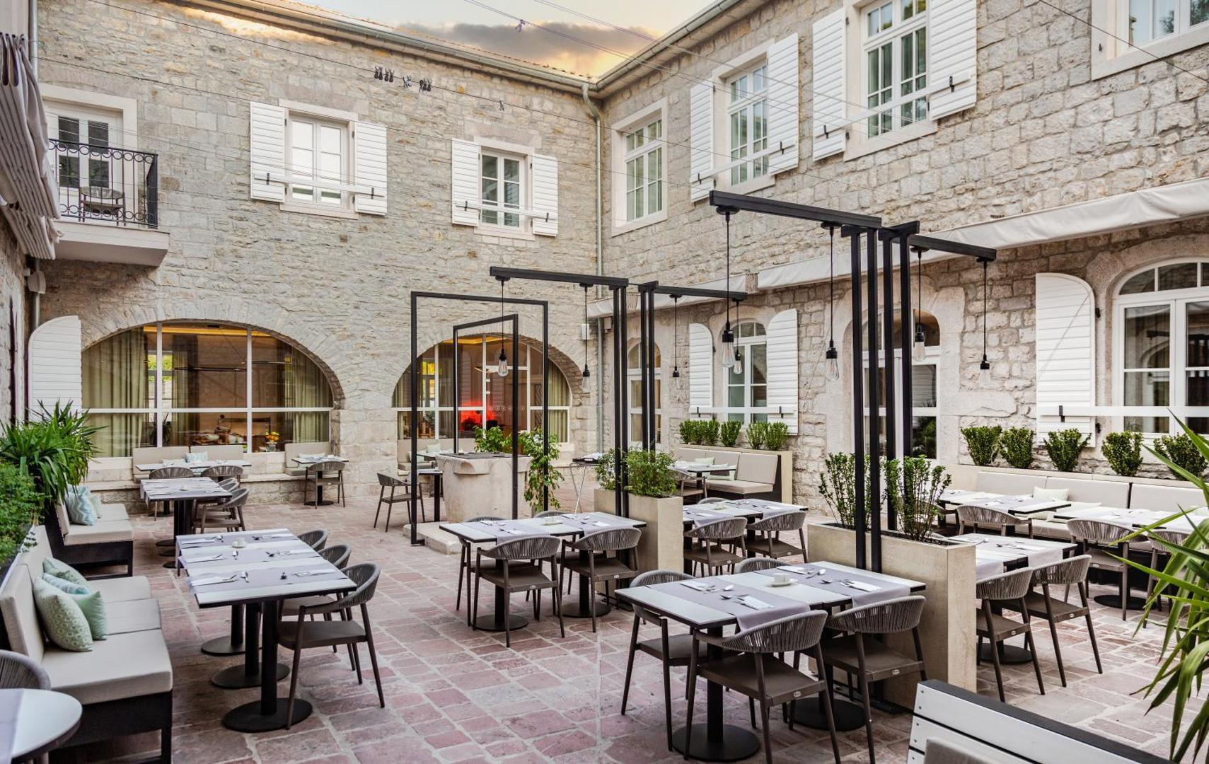 Lazure Hotel & Marina vēsturiskais iekšpagalms ar restorāna galdiem un akmens mūra arhitektūru Melnkalnē
